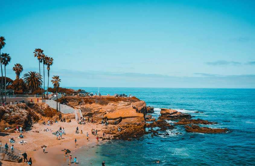 Em um dia ensolarado, praia de San Diego, uma das cidades para conhecer nos Estados Unidos com árvores e pessoas ao redor
