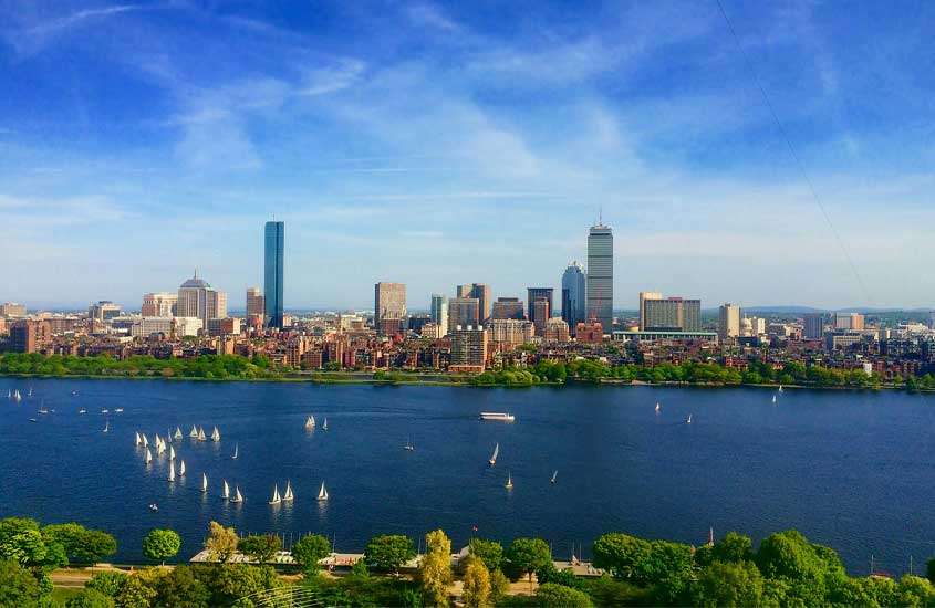 Em um dia de sol, paisagem de Boston, uma das cidades para conhecer nos Estados Unidos com barcos, árvores e prédios ao redor