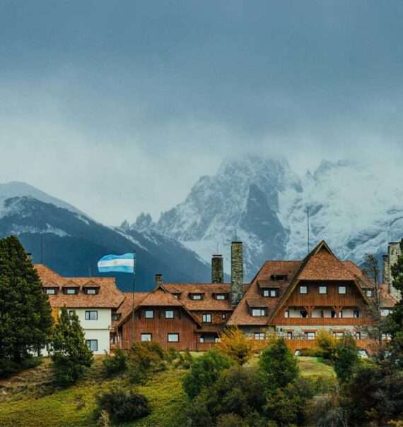 Em um dia nublado, um dos hotel de Bariloche com árvores ao redor e montanhas atrás