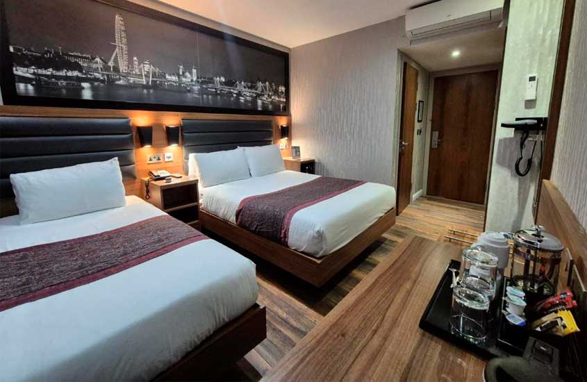 Suíte espaçosa de um dos melhores hotéis em londres para brasileiros, com duas camas de casal, quadro decorativo e chaleira