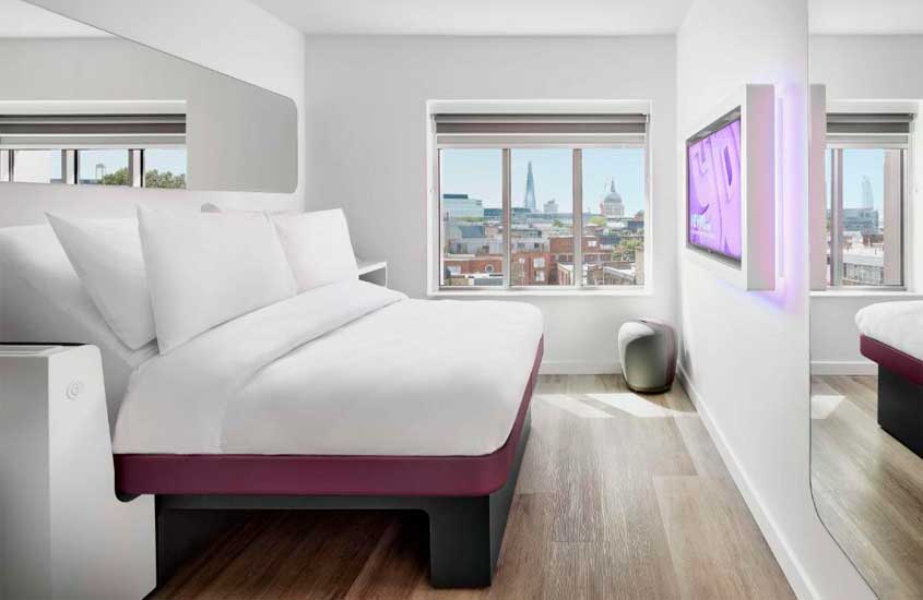 Suíte minimalistade hotel com TV, janela, cama de casal e espelhos
