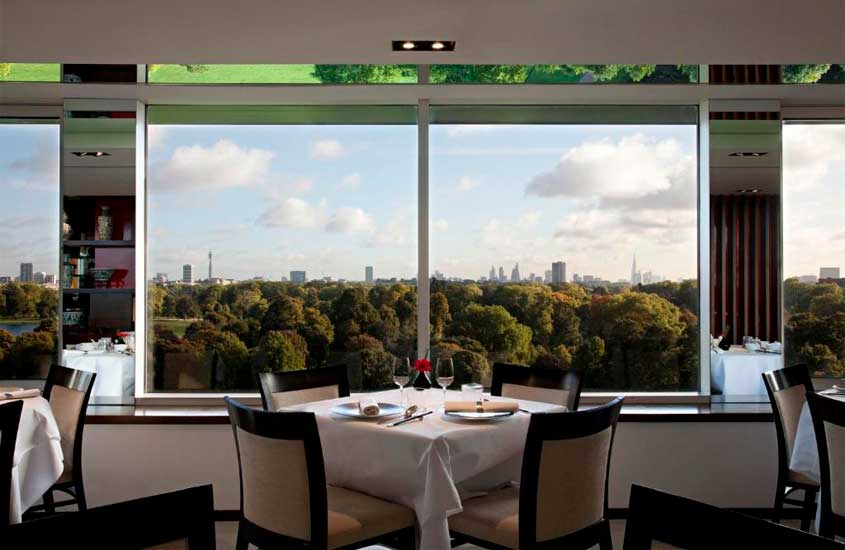 Restaurante com vista de um dos melhores hotéis em londres para brasileiros, com mesas postas, cadeiras e janelas grandes