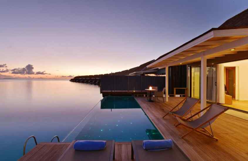 Durante o entardecer, deck de um hotel romântico nas Maldivas com espreguiçadeiras, piscina e mar do lado