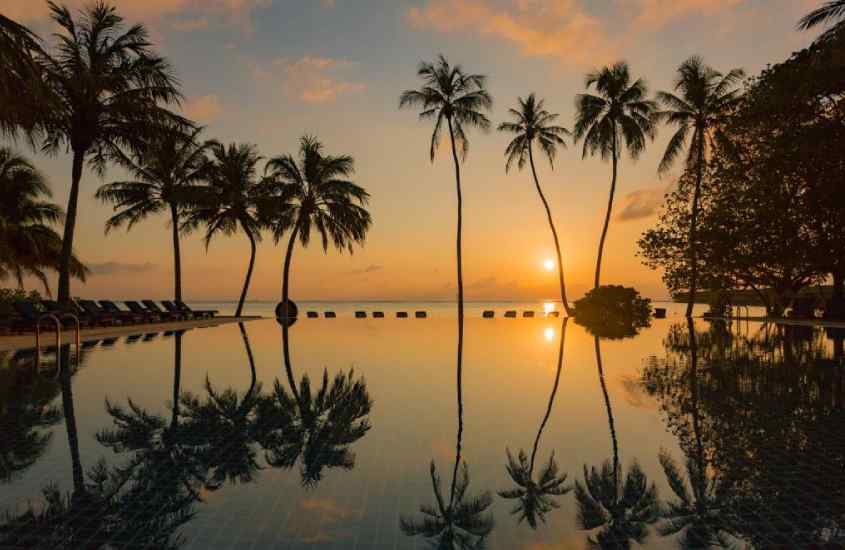 Durante o pôr do sol, área de lazer de um hotel para passar a lua de mel nas Maldivas com piscina, espreguiçadeiras e árvores ao redor