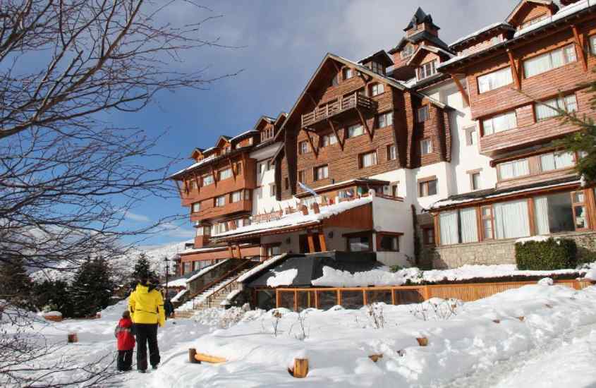 Em um dia de sol com nuvens, fachada de um dos melhores hotéis em Bariloche para família com árvores e partes nevadas