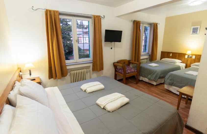 Quarto de um dos melhores hotéis em Bariloche para família com camas confortáveis, moveis de madeira e janelas acortinadas