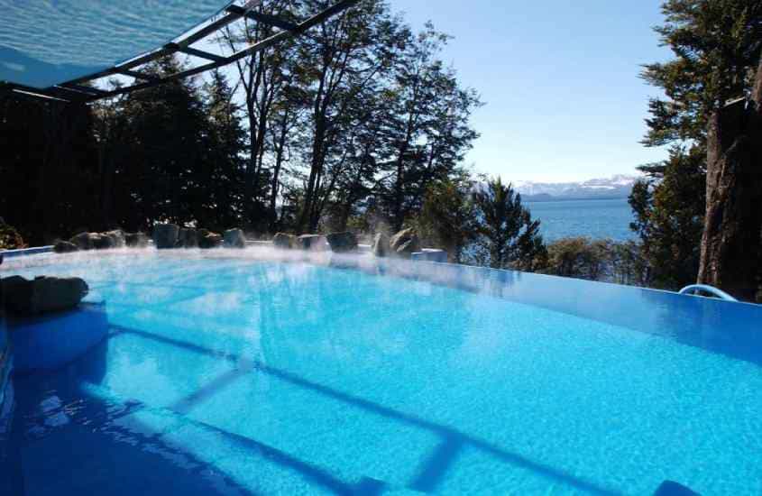 Em um dia de sol, área de lazer de um dos melhores hotéis em Bariloche para família com piscina e árvores ao redor