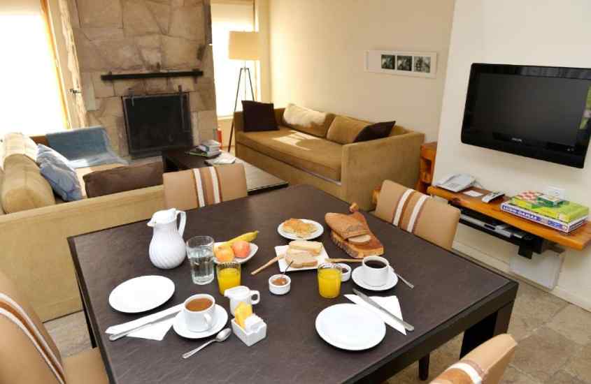 Sala de dois ambientes de um dos melhores hotéis em Bariloche para família, com sofás, lareira, TV e mesa com cadeiras