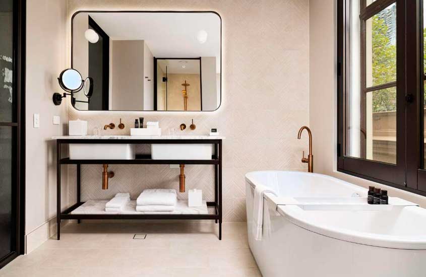 Banheiro de um hotéis onde ficar em Melbourne com banheira, toalhas, pias, espelhos e janela do lado