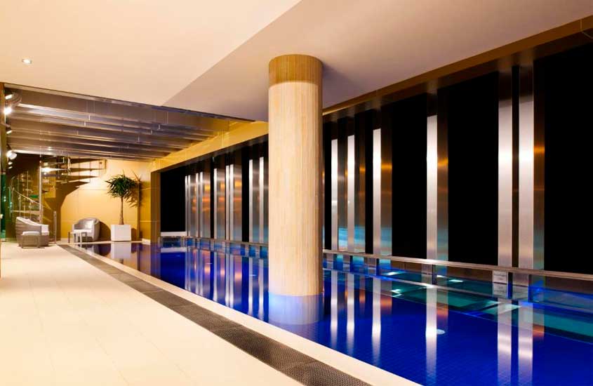 Área de lazer coberta de um dos hotéis onde ficar em Melbourne, com piscina, poltronas, janelas grandes e planta decorativa