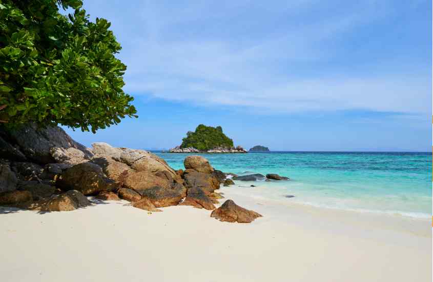 Em um dia ensolarado, praia de Koh Lipe com areia branca, águas cristalinas e árvores do lado com rochas