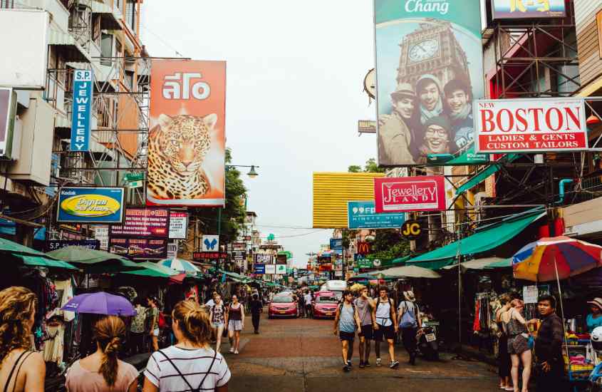 Em um dia nublado, Khao San Road, um dos pontos turísticos da Tailândia com diversas lojas, carros e pessoas ao redor