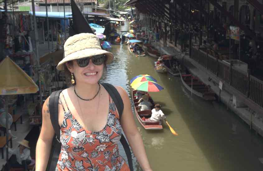 Em um dia de sol, Bárbara Rocha Alcantelado em Damnoen Saduak, um dos principais pontos turísticos da Tailândia, com mercado atrás e pessoas em embarcações