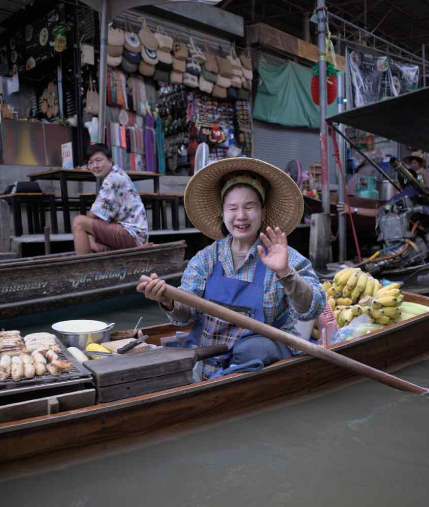 Em um dia de sol, tailandesa em barco com mercado atrás