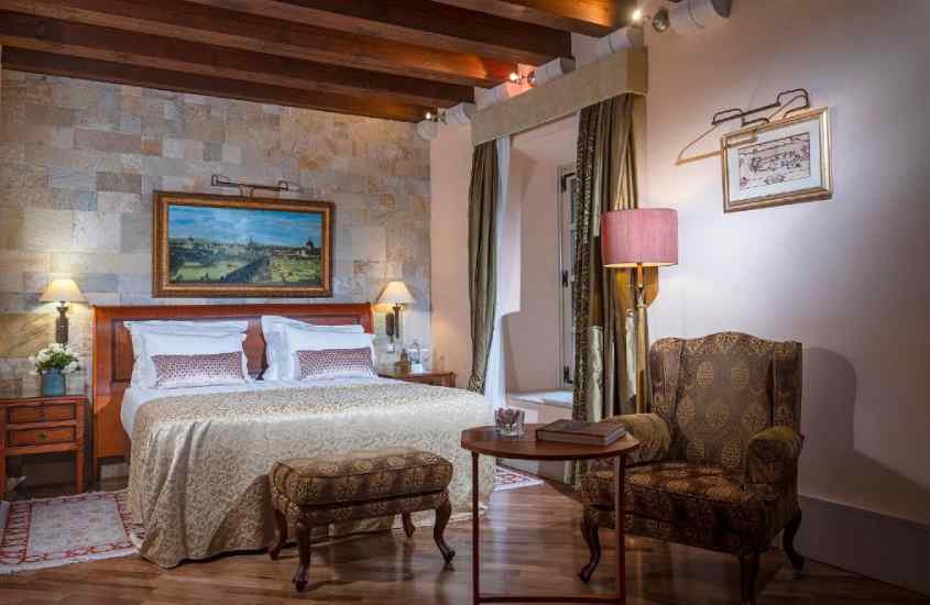 Quarto de um hotel em Dubrovnik com cama de casal, quadros decorativos, janelas grandes, poltronas, tapetes, mesas e luminárias