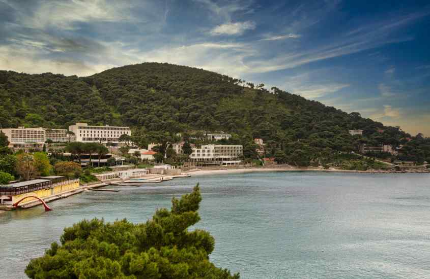 Durante o entardecer, paisagem de Lapad um dos bairros onde ficar em Dubrovnik com casas, praia e árvores ao redor