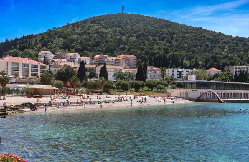 Em um dia de sol, praia de Babin Kuk, com casas e árvores atrás