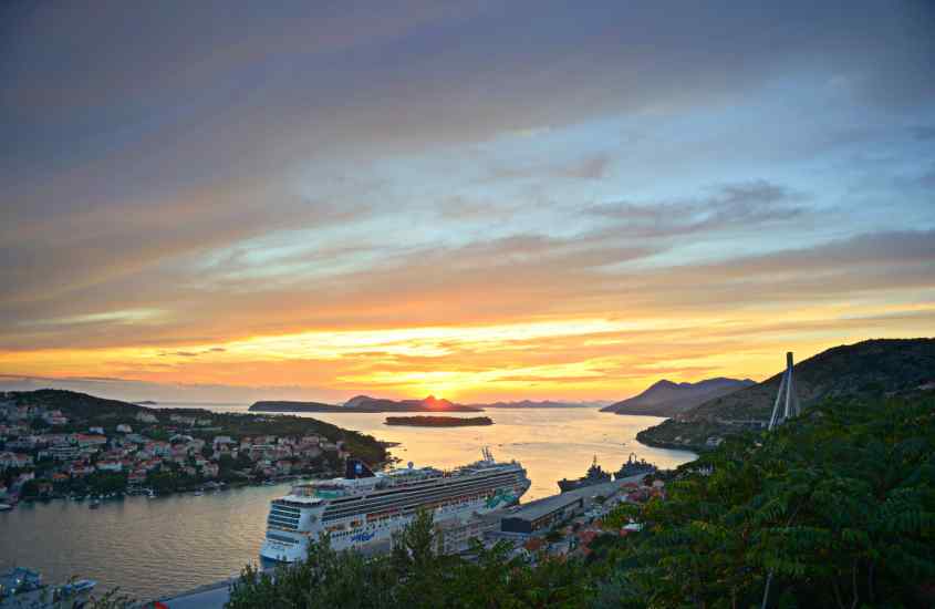 Durante o pôr do sol, visão aérea do Porto Gruz com mar, árvores, navio e casas ao redor