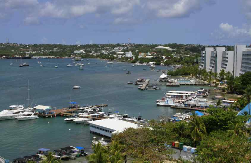 Em um dia de sol, paisagem da cidade de San Andres com árvores e casas atrás e mar com barcos na frente