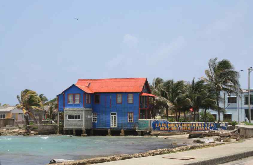 Em um dia de sol, casa colorida de um dos bairros onde ficar em San Andres, com árvores ao redor e praia do lado