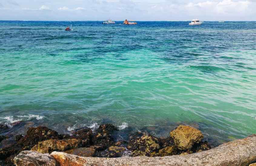 Em um dia ensolarado, praia de um dos lugares onde ficar em San Andres com pedras e barcos no fundo