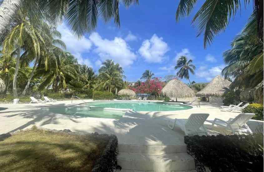 Em um dia de sol, área de lazer de um dos hotéis em San Andres com piscina, tenda de palha, espreguiçadeiras, plantas e árvores ao redor