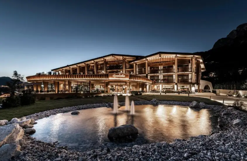 Fachada do hotel Granbaita Dolomites iluminada à noite, com uma fonte na área externa