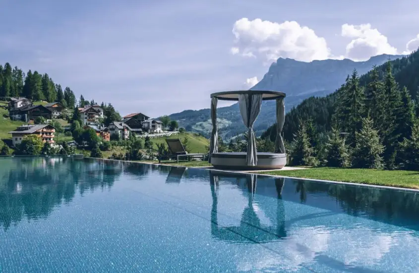 Piscina infinita em La Villa com montanhas ao fundo e vilas alpinas ao redor durante o dia