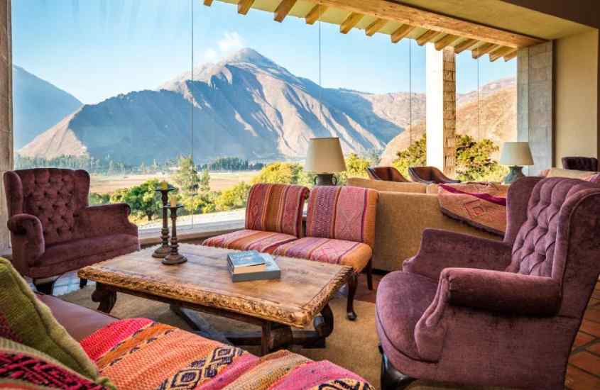 Lounge de um dos hotéis onde se hospedar em machu picchu com mesas, cadeiras, poltronoas, sofás, janelas e paisagem das montanhas