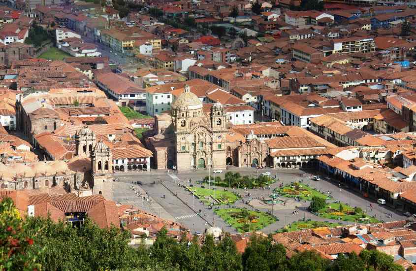 Em um dia de sol, praça de Cusco uma cidade próxima a machu picchu com casas, construções e árvores ao redor