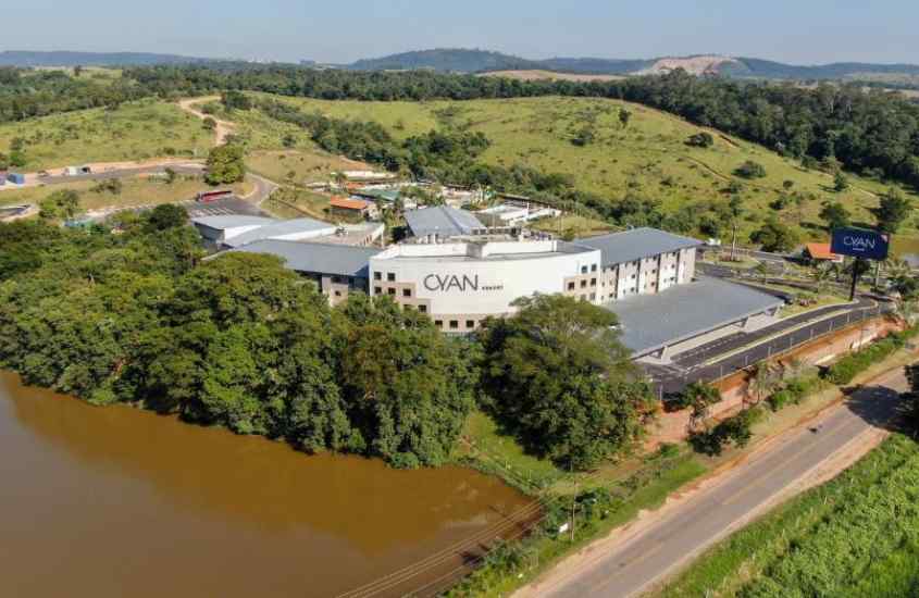 Em um dia ensolarado, visão aérea de um hotel com lago e árvores ao redor