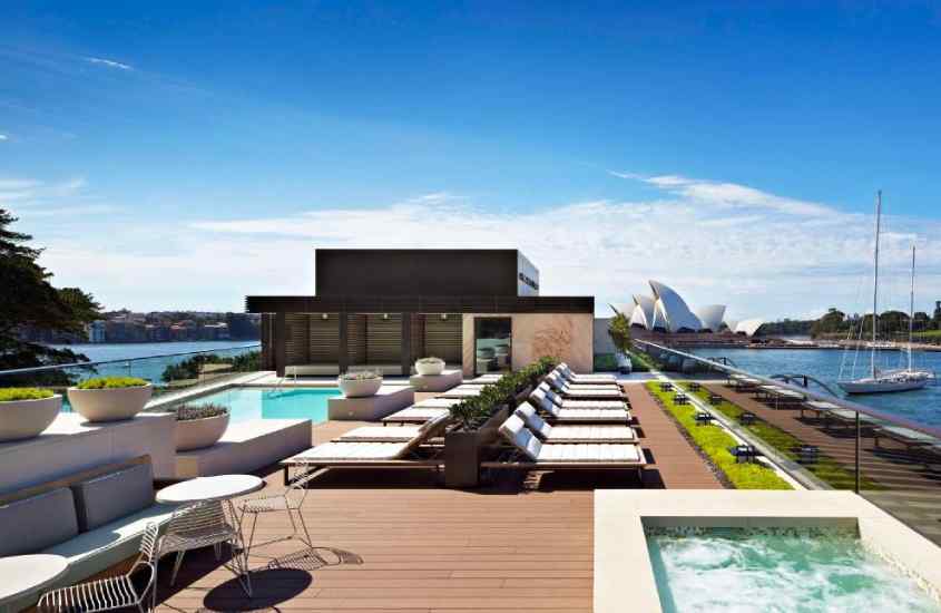 Em dia de sol, área de lazer de um hotel onde passar reveillon em Sydney, com piscinas, banheiras, espreguiçadeiras, mesas, cadeiras, árvores e parte gramada