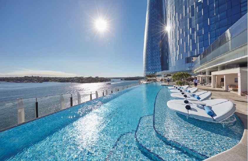 Em um dia de sol, área de lazer de um hotel com piscina grande espreguiçadeiras e mar do lado