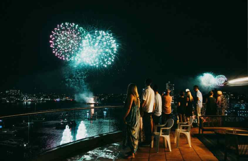 Durante a noite, queima de fogos do Réveillon em Sydney, com pessoas assistindo