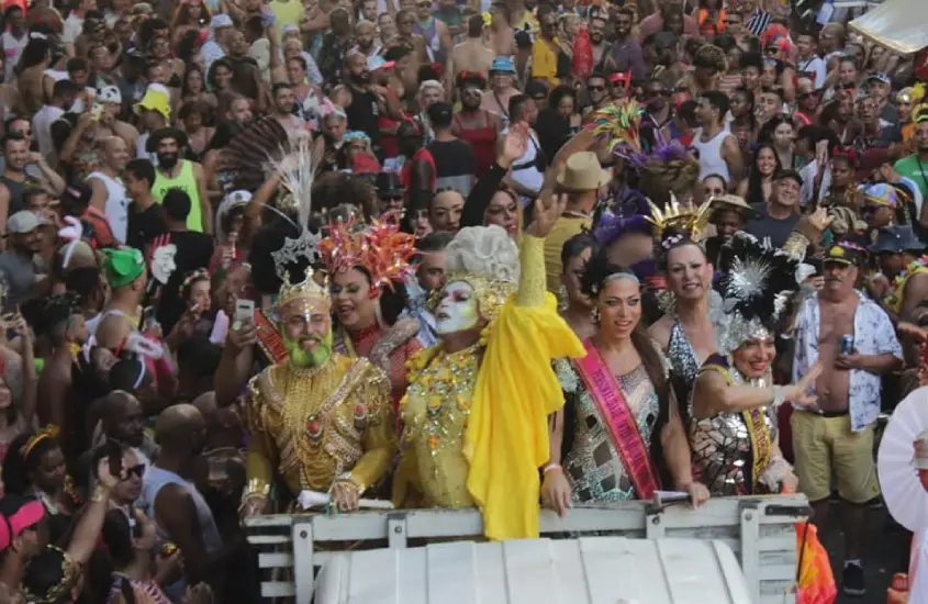 Foliões e performers em fantasias vibrantes desfilam no Bloco Banda das Quengas, com uma multidão animada ao redor