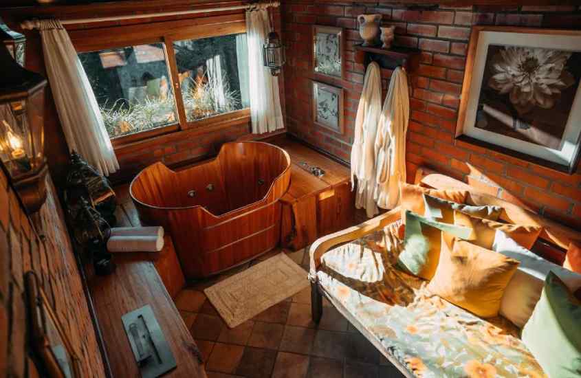 Quarto de hotel vinícola no Vale dos Vinhedos com banheira de madeira, sofá, quadros decorativos, janelas grandes e tapetes