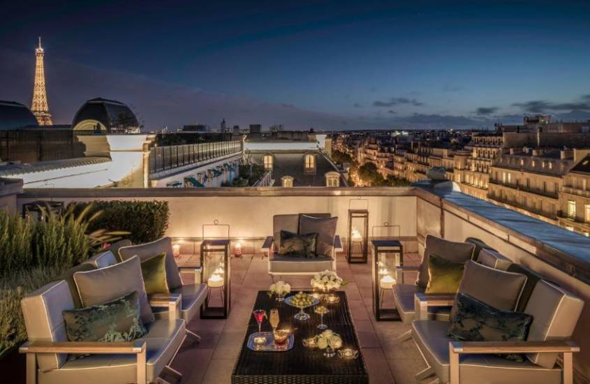 Durante a noite, cobertura de um hotel de luxo em Paris com mesas, cadeiras, plantas decorativas e paisagem da cidade no fundo