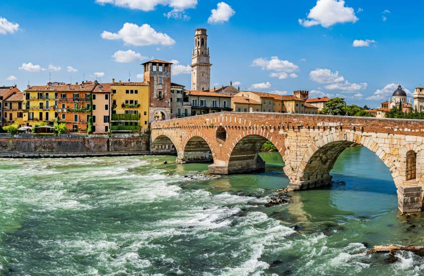 Em um dia de sol, Verona com ponte, prédios históricos e árvores ao redor