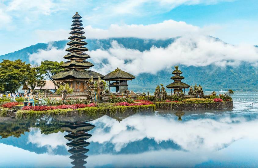 Em um dia de sol, paisagem de Bali com árvores, templos, plantas decorativas, rio ao redor e montanhas atrás