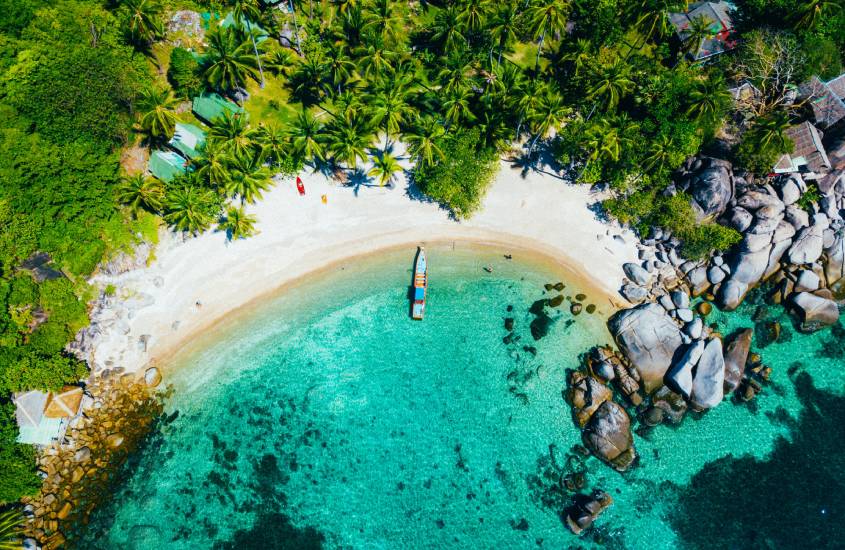 Em um dia ensolarado, praia de Koh Samui com árvores ao redor, pedras e mar do lado