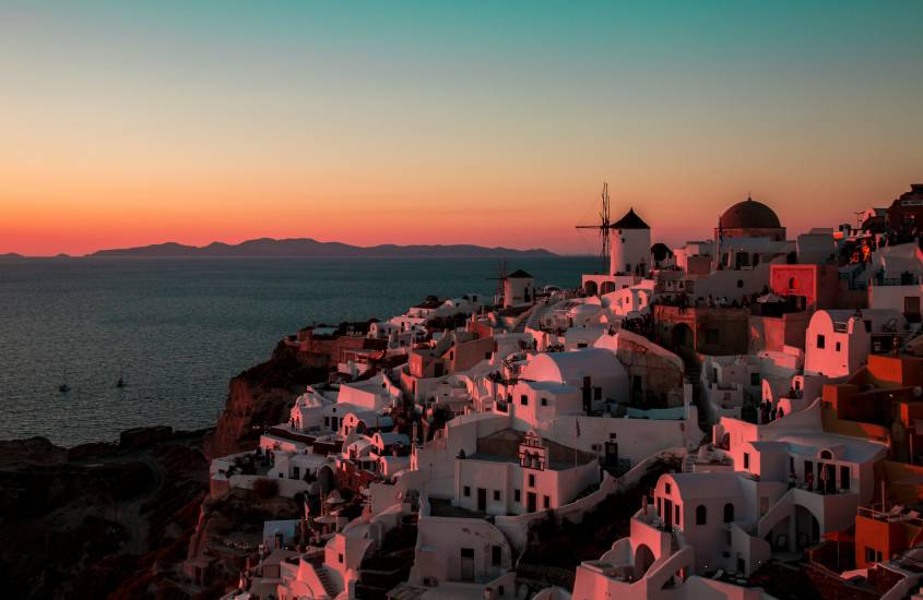 Durante o entardece, paisagem de Santorini, um dos lugares para passar a lua de mel com casinhas brancas e litoral dos lados