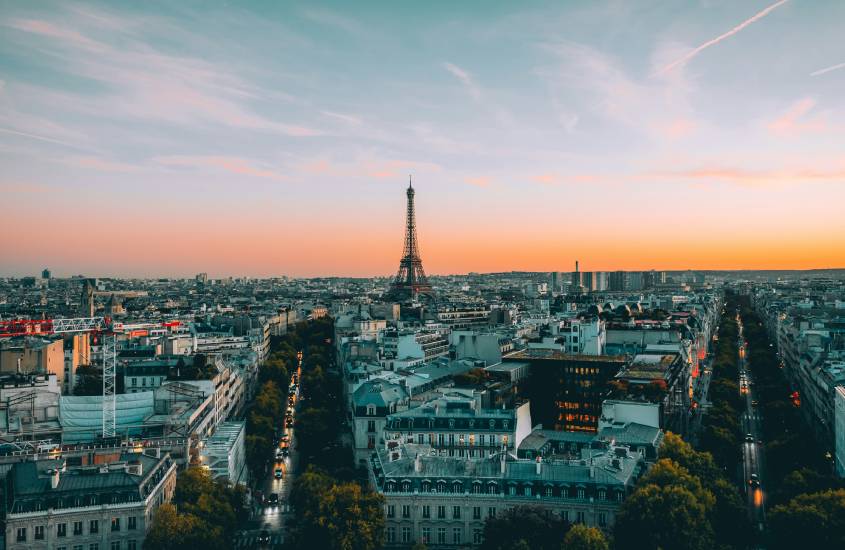 Durante o entardecer, paisagem de Paris, um dos lugares para passar a lua de mel com torre eiffel no meio, prédios e árvores ao redor