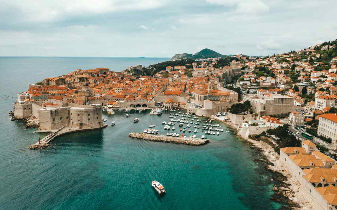 Em um dia nublado, vista aérea de Dubrovnik com praia, barcos, casas e árvores ao redor