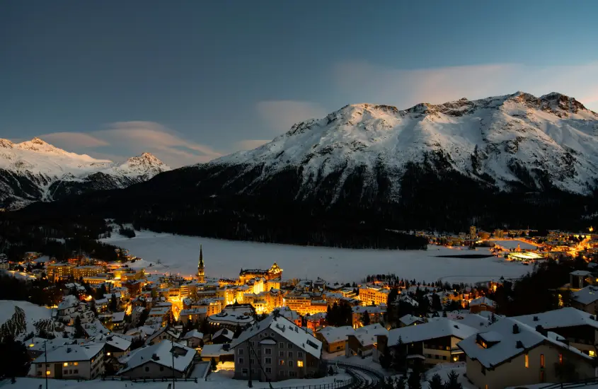 Vista noturna de St. Moritz com luzes da cidade e montanhas cobertas de neve