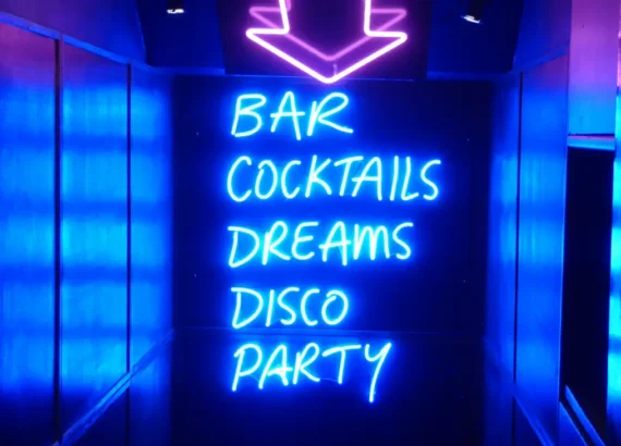 Neon azul vibrante com as palavras 'Bar, Cocktails, Dreams, Disco, Party', iluminando um corredor escuro, criando um convite tentador para uma noite de festa