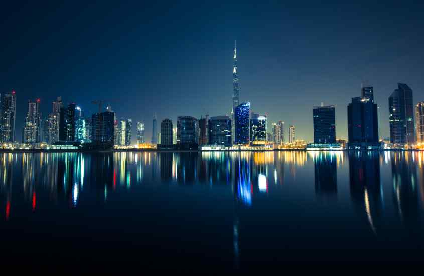 Durante a noite, cidade de Dubai iluminada e refletida no mar