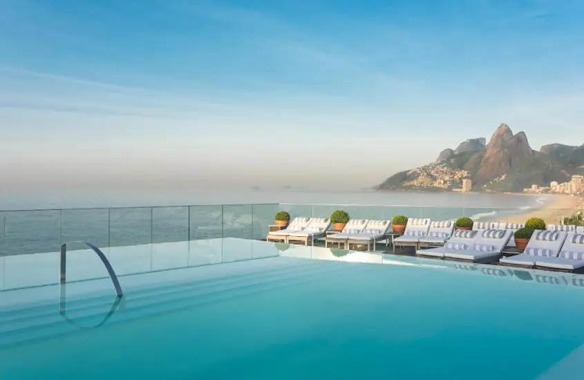 Vista panorâmica da piscina infinita do Hotel Fasano Rio de Janeiro com o mar e montanhas ao fundo durante o dia.