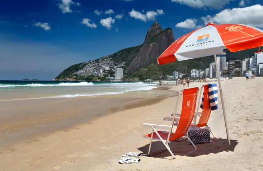 Cadeiras e guarda-sol do Mar Ipanema Hotel na Praia de Ipanema com o mar e montanhas ao fundo durante o dia