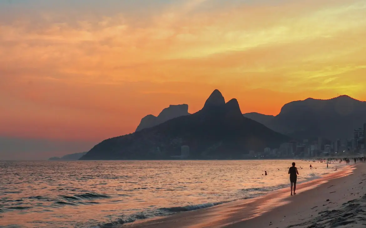 Pôr do sol na Praia de Ipanema, Rio de Janeiro, com o Morro Dois Irmãos ao fundo, refletindo tons de laranja e rosa no céu e no mar