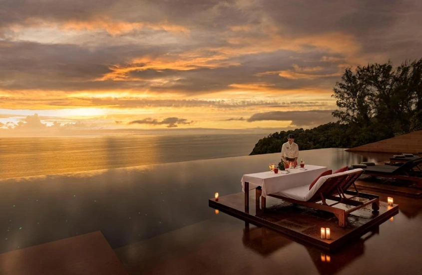 Mesa de jantar ao lado de uma piscina infinita com vista para o mar e o pôr do sol em Phuket, Tailândia